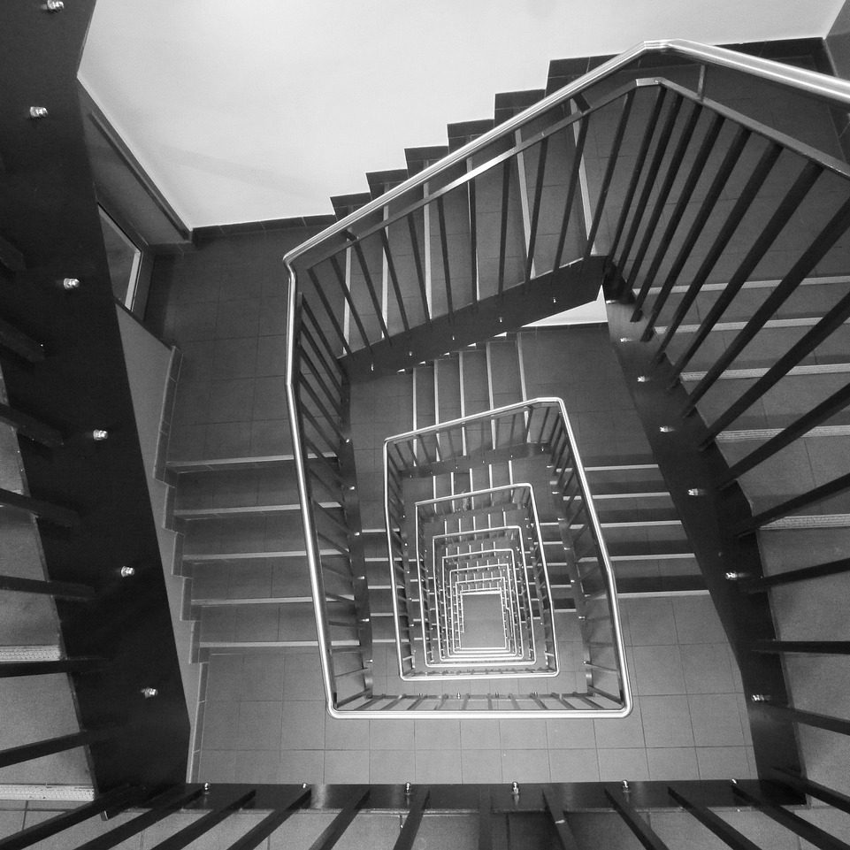 Schwarz-weiß Bild einer sich spiralartig wunden Treppe mit Geländer.