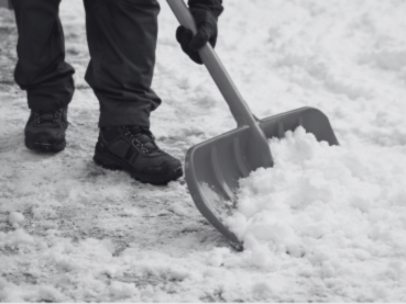 Person mit Schaufel, die Schnee von einem Weg räumt.