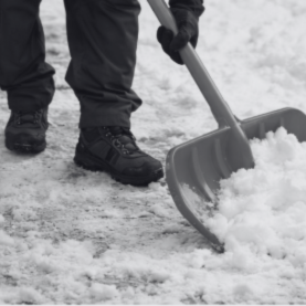 Eine Person schaufelt Schnee mit einer großen Schaufel auf dem Boden.
