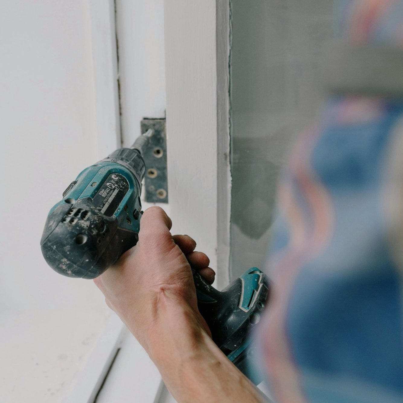 Hand hält einen Akku-Schrauber, während an einem Fenster gearbeitet wird.