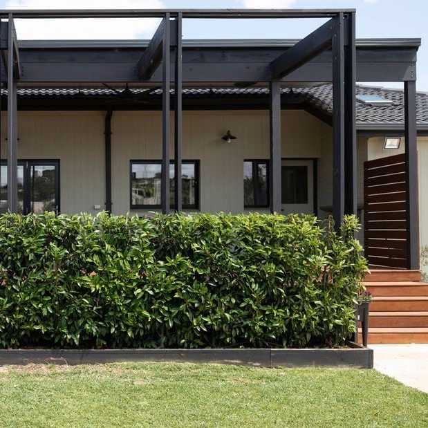 Modernes Haus mit schwarzem Überstand, grüner Hecke und Treppe im Vordergrund.